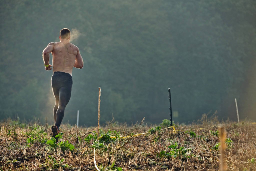 Man running through field during obstacle course race.