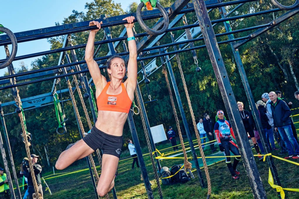 Woman in orange swinging through monkey bars in obstacle course using mental toughness to power through.