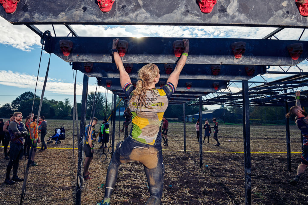 woman hanging from a traverse obstacle during an obstacle course race